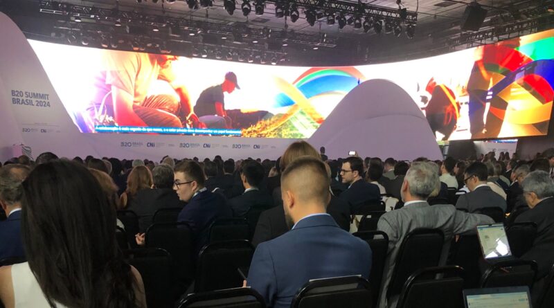 Auditório com pessoas sentadas olhando para o palco que passa vídeo de apresentação.