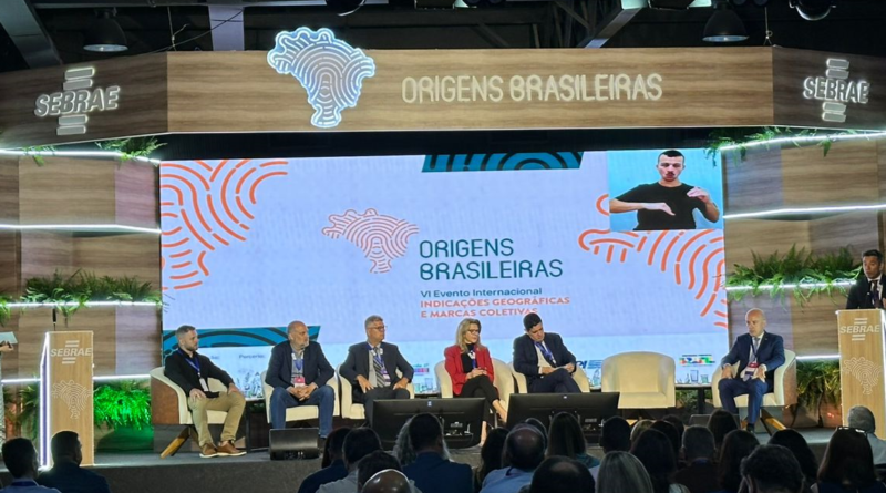 Evento em que há cinco pessoas sentadas e duas em pé, uma em cada lado do palco.