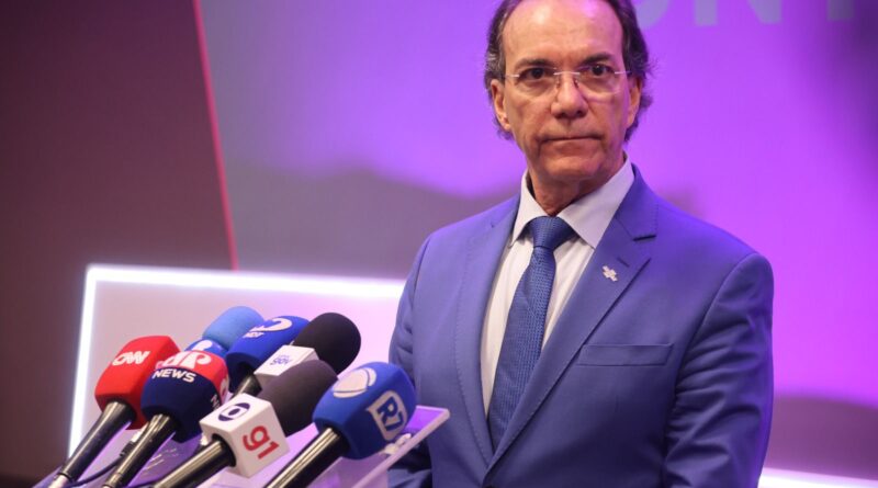 Homem em pé com terno azul e fundo neutro