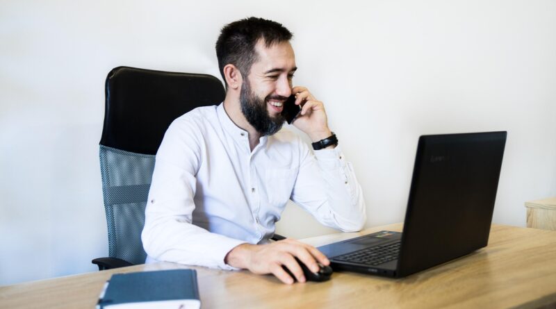 Homem sentado em uma cadeira, sobre a mesa há um notebook e uma agenda