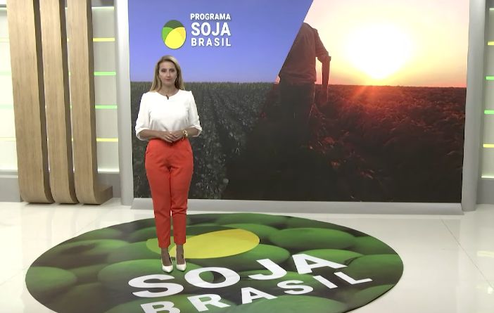 Apresentadora com camisa branca e calça laranja no estúdio do Soja Brasil