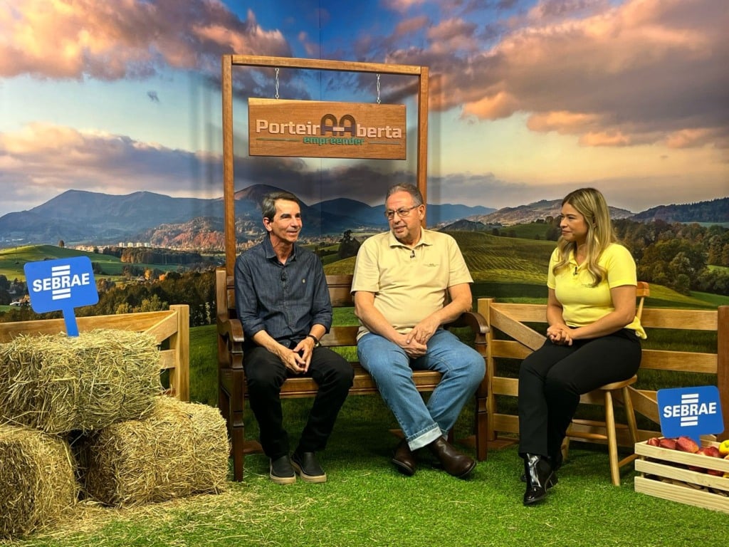 Três pessoas sentadas com o cenário de uma fazenda 