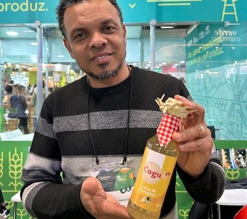 homem de barba sorrindo, segurando com as duas mãos uma garrafa de licor na cor amarela e ornamentada com chapéu de palha