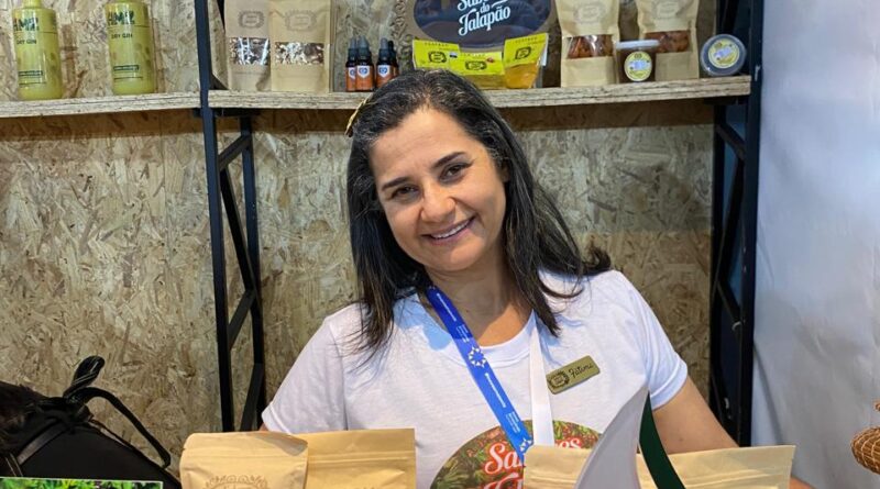 Uma mulher que tem à sua frente uma bancada repleta de produtos que ela produz no Jalapão, Tocantins. A foto. é arquivo pessoal e foi tirada em uma feira que aconteceu em Macapá, Amapá