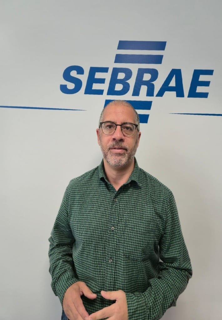 Na foto, há um homem com camisa verde. No fundo da foto, está o logo do Sebrae