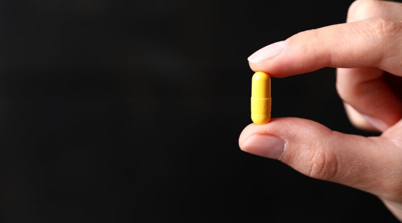 Mão segurando pílula que parece ser de cúrcuma, suplemento alimentar