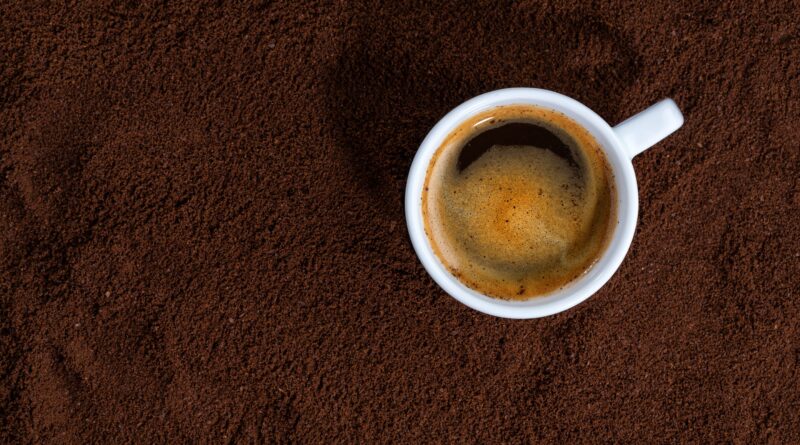 Imagem mostra xícara de café com a bebida em cima café moído