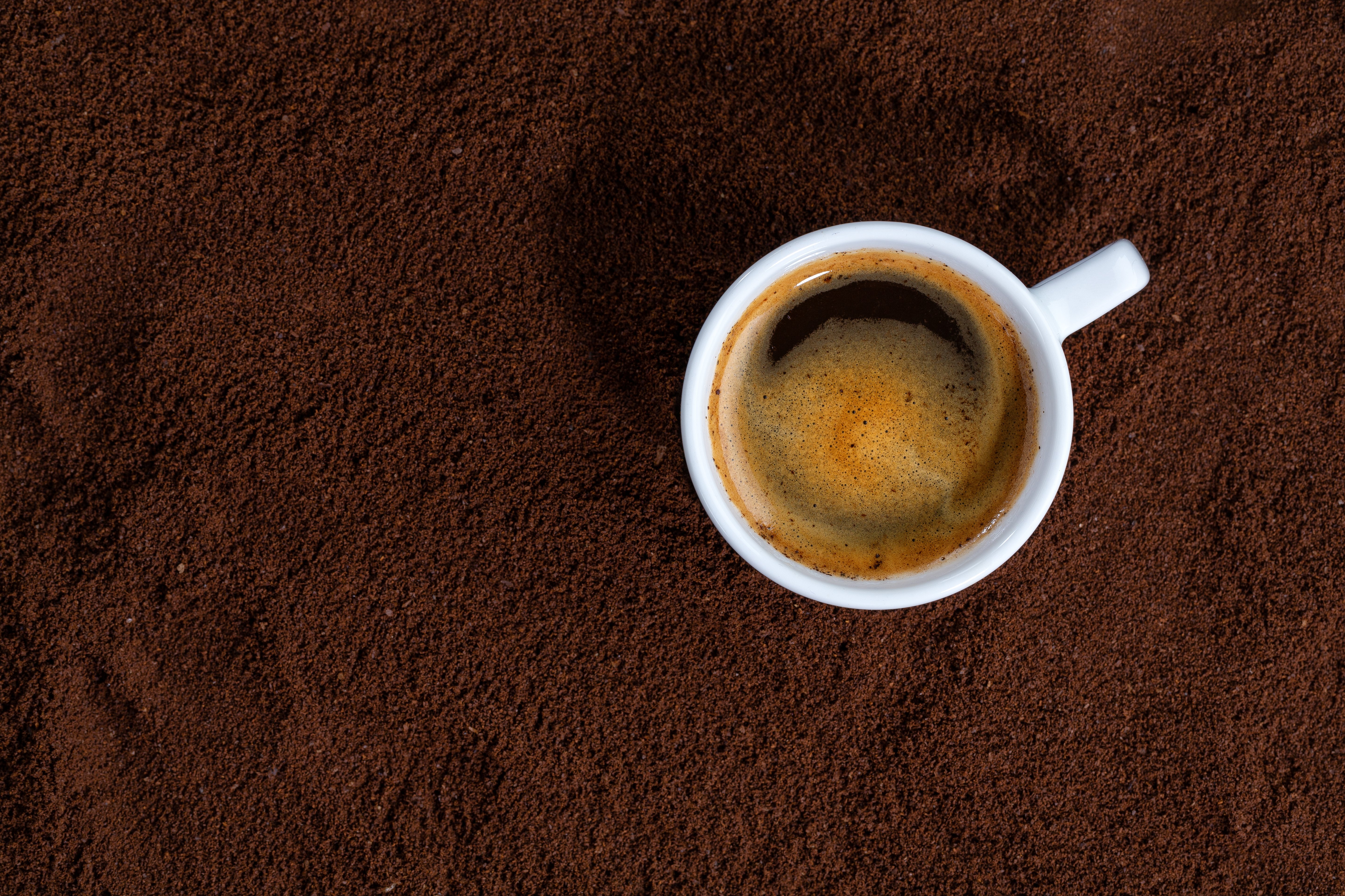 Imagem mostra xícara de café com a bebida em cima café moído